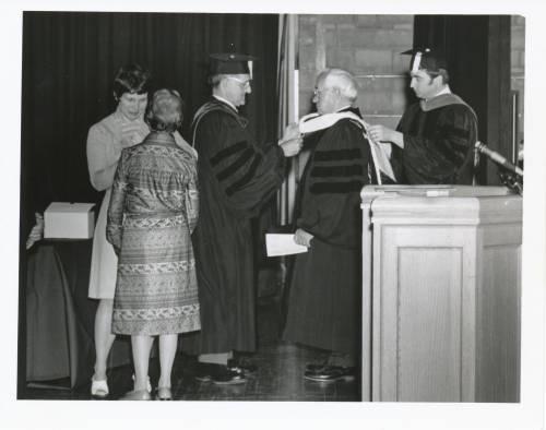 
President L.L. Ramseyer receives a hood and the honorary Doctor of Humane Letters degree from Bluffton University at the 1976 commencement. Pictured are Howard Raid and President Benjamin Sprunger.